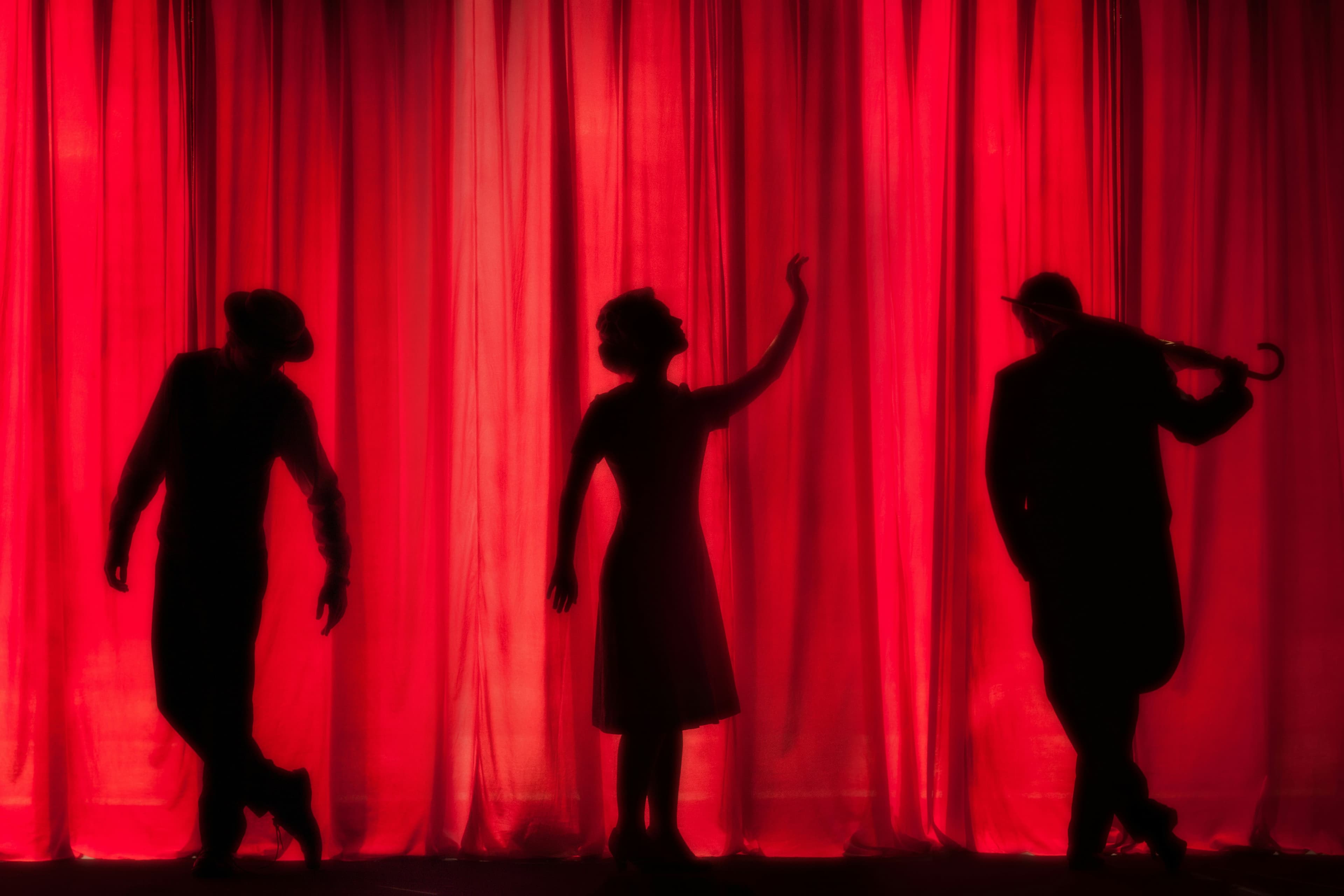 Silhouetted actors against a red theatre curtain